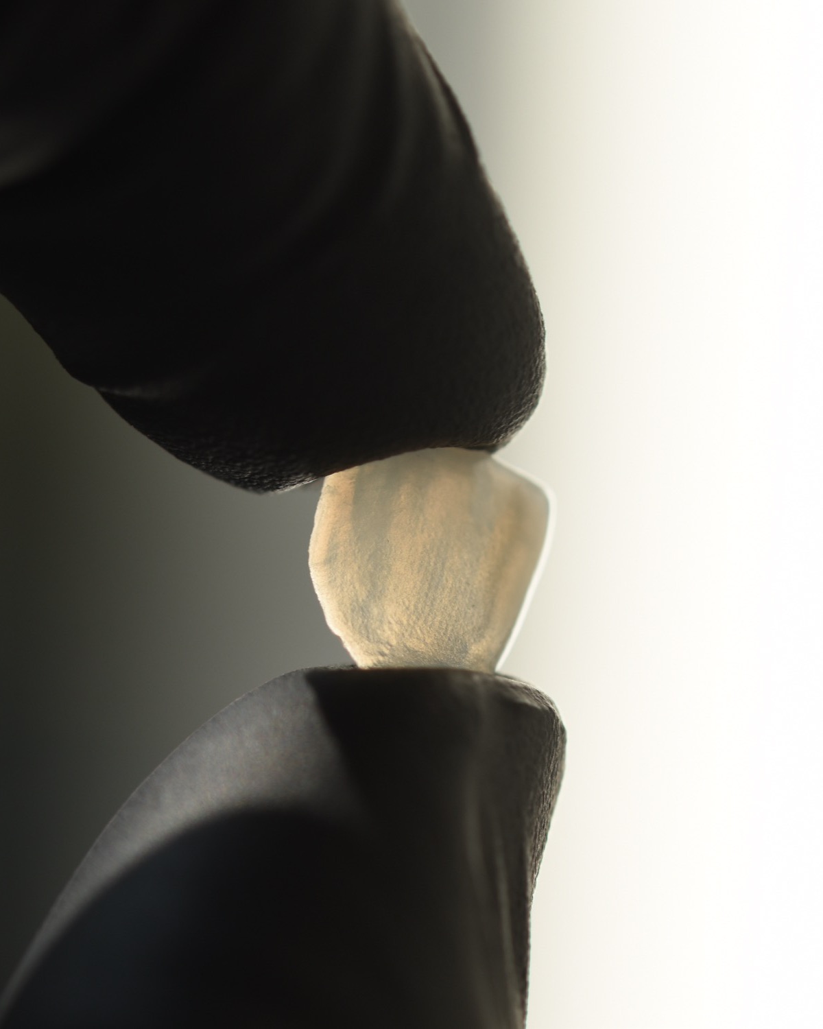 Carilla de cerámica de espesor mínimo sostenida entre los dedos antes de su terminación manual